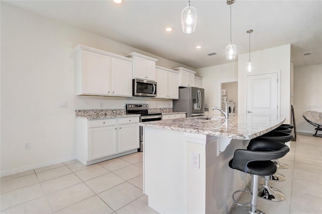 kitchen with a center island with sink, white cabinets, appliances with stainless steel finishes, decorative light fixtures, and a kitchen bar