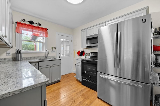 kitchen with gray cabinetry, light stone counters, light wood-type flooring, appliances with stainless steel finishes, and sink