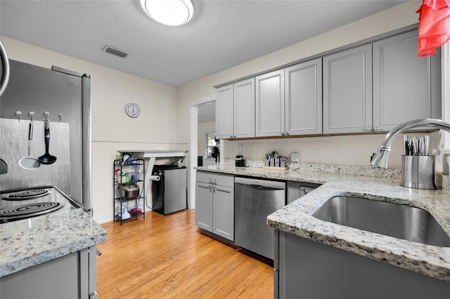 kitchen featuring light stone counters, dishwasher, sink, gray cabinets, and light hardwood / wood-style flooring