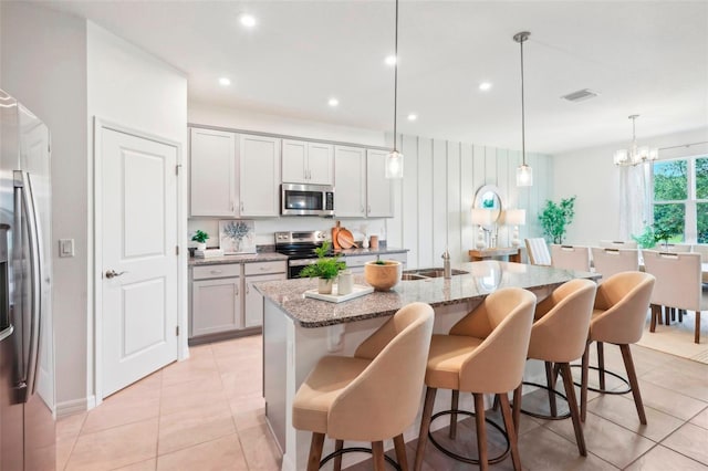 kitchen with a kitchen bar, stainless steel appliances, a center island with sink, light stone countertops, and pendant lighting