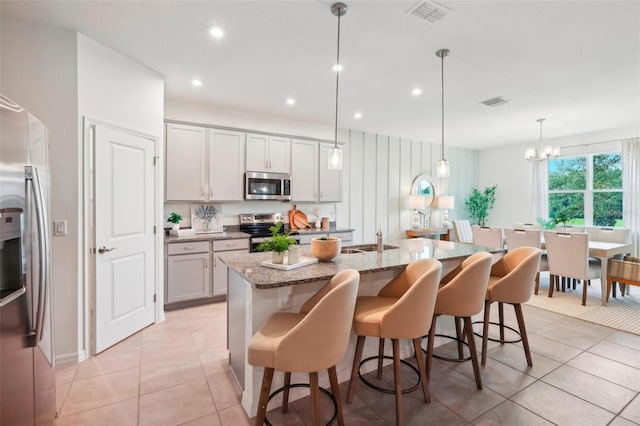 kitchen featuring stainless steel appliances, a breakfast bar area, an island with sink, and decorative light fixtures