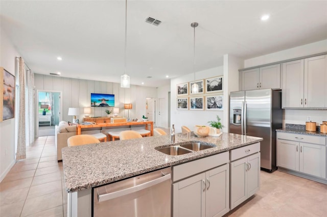 kitchen featuring stainless steel appliances, a center island with sink, sink, hanging light fixtures, and gray cabinets