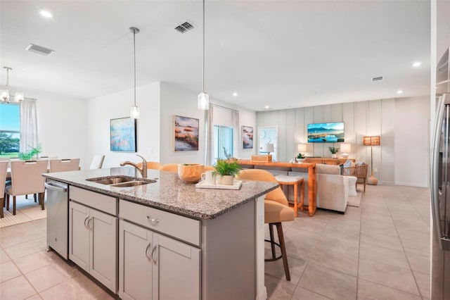 kitchen featuring light tile patterned flooring, light stone countertops, hanging light fixtures, sink, and a kitchen island with sink