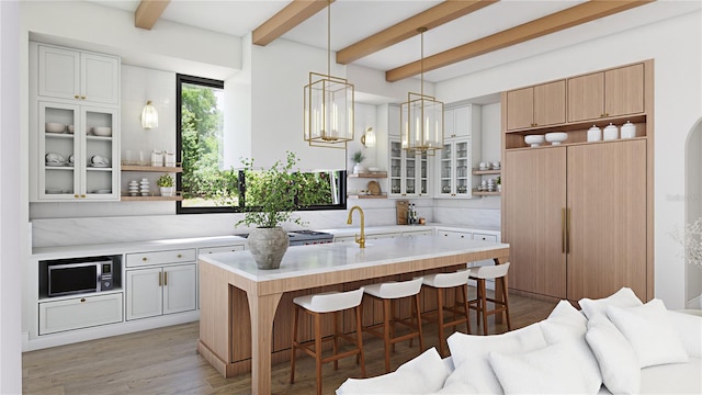 kitchen featuring hardwood / wood-style floors, beam ceiling, a kitchen island with sink, a kitchen breakfast bar, and white cabinets