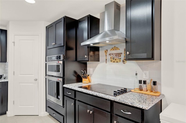 kitchen featuring decorative backsplash, light stone countertops, wall chimney exhaust hood, black electric cooktop, and double oven