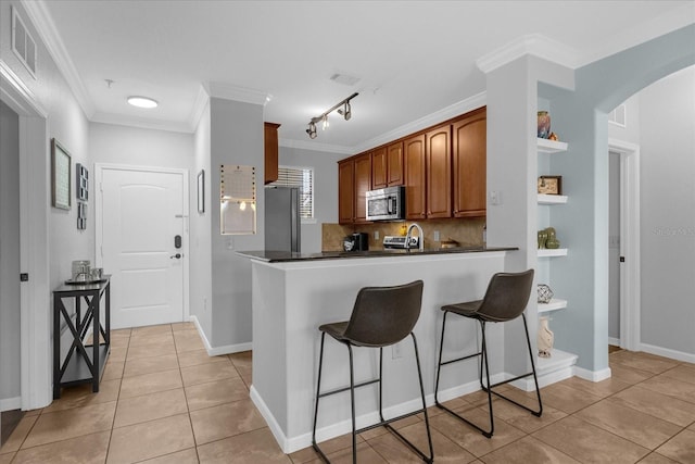 kitchen with crown molding, stainless steel appliances, light tile patterned floors, decorative backsplash, and kitchen peninsula