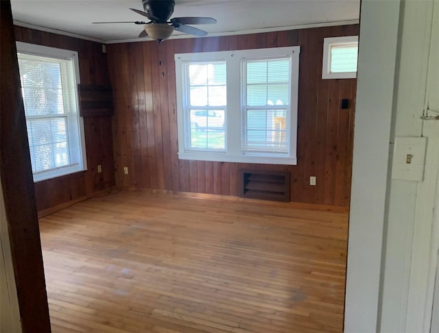 empty room with ceiling fan, wooden walls, and light hardwood / wood-style floors