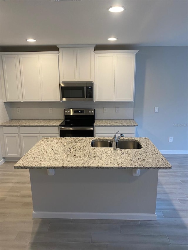 kitchen featuring sink, stainless steel appliances, an island with sink, wood-type flooring, and white cabinets