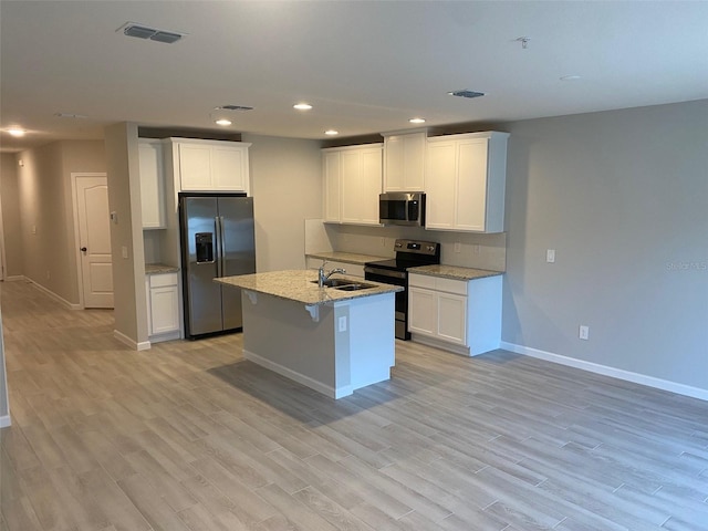 kitchen with stainless steel appliances, a kitchen island with sink, sink, light hardwood / wood-style floors, and white cabinetry