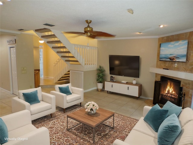 living room featuring ornamental molding, a textured ceiling, light tile patterned floors, a large fireplace, and ceiling fan