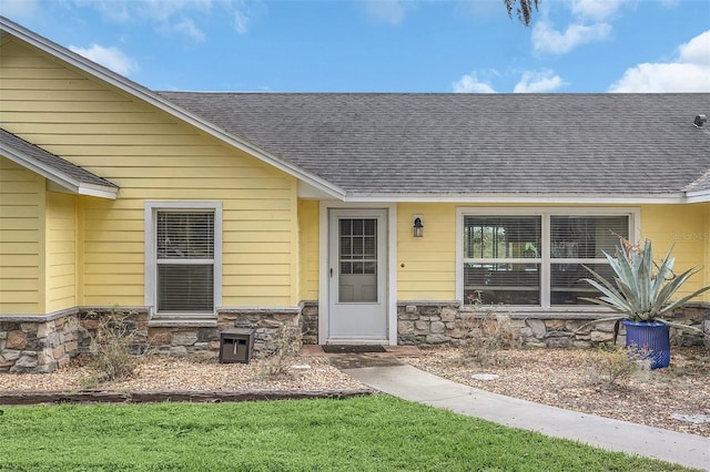 doorway to property featuring stone siding and a shingled roof