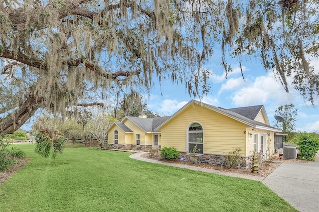 ranch-style home with central air condition unit, a front yard, stone siding, and roof with shingles
