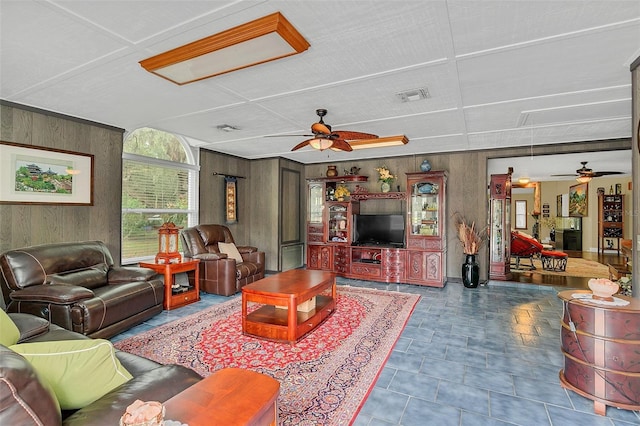 living room featuring ceiling fan, wooden walls, and attic access