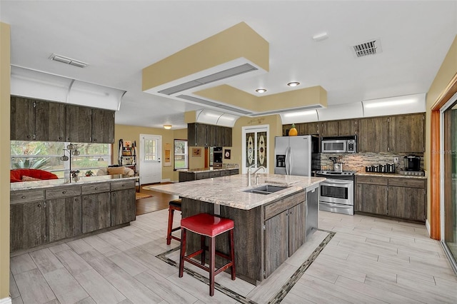 kitchen with appliances with stainless steel finishes, a sink, a kitchen bar, dark brown cabinetry, and backsplash