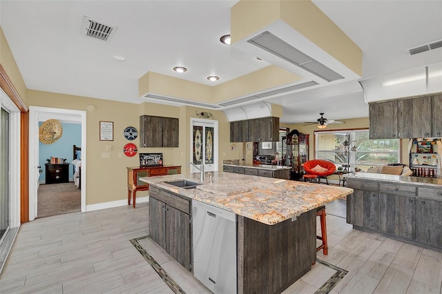 kitchen featuring a sink, a raised ceiling, ceiling fan, dark brown cabinetry, and a kitchen island with sink