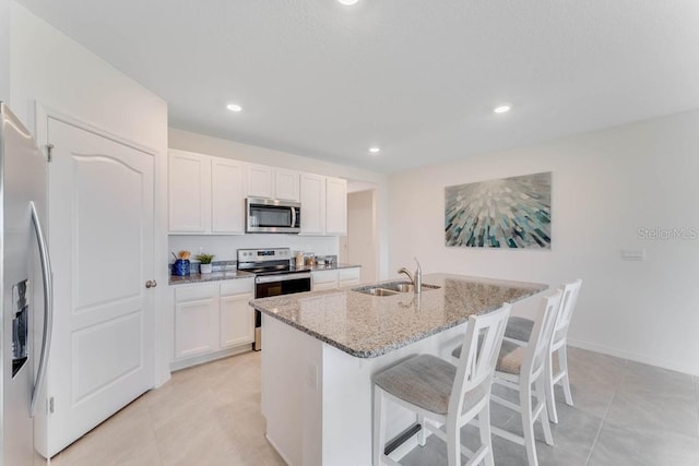 kitchen featuring sink, stainless steel appliances, light stone counters, white cabinets, and a center island with sink