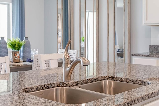 interior details featuring light stone countertops, sink, and white cabinets