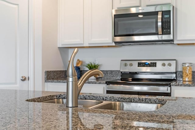 kitchen featuring stainless steel appliances, white cabinetry, and dark stone counters