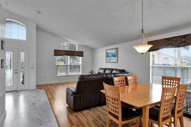 dining space with plenty of natural light, light hardwood / wood-style flooring, lofted ceiling, and a textured ceiling