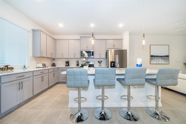 kitchen with stainless steel appliances, hanging light fixtures, a kitchen island with sink, a kitchen breakfast bar, and backsplash