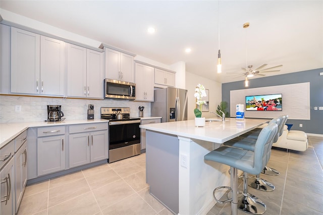 kitchen with sink, appliances with stainless steel finishes, decorative light fixtures, a kitchen island with sink, and decorative backsplash