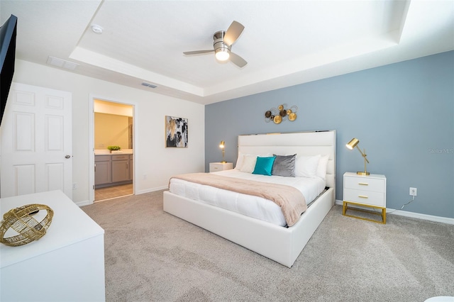 carpeted bedroom featuring ensuite bath, ceiling fan, and a raised ceiling