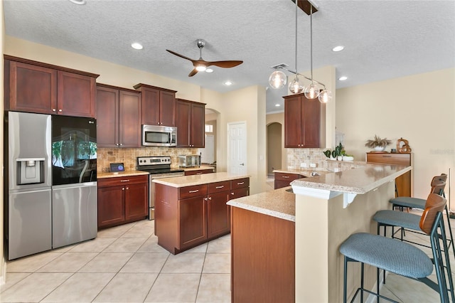 kitchen featuring stainless steel appliances, a textured ceiling, hanging light fixtures, kitchen peninsula, and ceiling fan