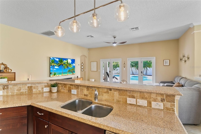 kitchen with french doors, hanging light fixtures, a textured ceiling, sink, and light stone countertops