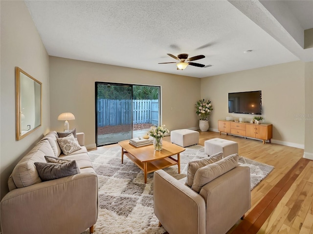 living room with ceiling fan, a textured ceiling, and light wood-type flooring