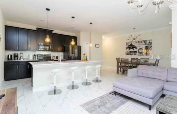 kitchen featuring pendant lighting, a kitchen island with sink, appliances with stainless steel finishes, a notable chandelier, and a kitchen bar