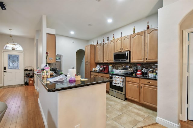 kitchen with stainless steel appliances, kitchen peninsula, hanging light fixtures, light hardwood / wood-style flooring, and decorative backsplash