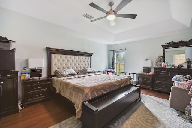 bedroom featuring dark wood-type flooring, a tray ceiling, and ceiling fan