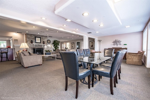 dining space with a stone fireplace, carpet, and a textured ceiling