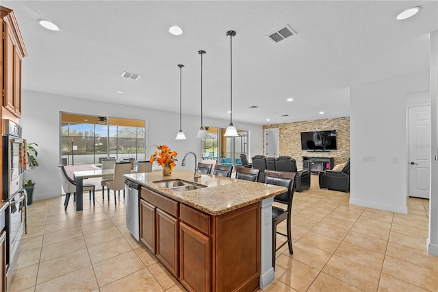 kitchen featuring light stone counters, stainless steel appliances, a stone fireplace, sink, and a kitchen island with sink