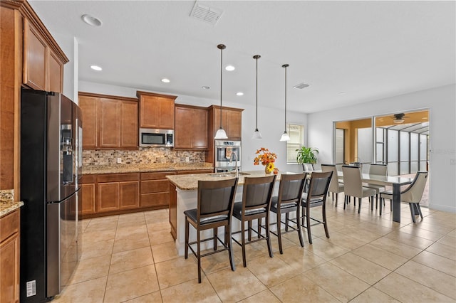 kitchen featuring hanging light fixtures, a breakfast bar area, an island with sink, light stone countertops, and appliances with stainless steel finishes