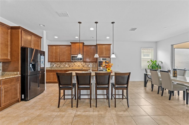 kitchen with light stone counters, appliances with stainless steel finishes, a breakfast bar area, decorative light fixtures, and an island with sink