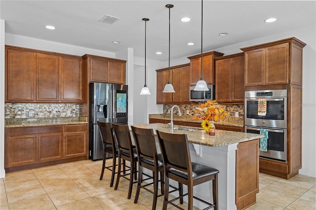 kitchen with a kitchen bar, decorative backsplash, an island with sink, appliances with stainless steel finishes, and decorative light fixtures