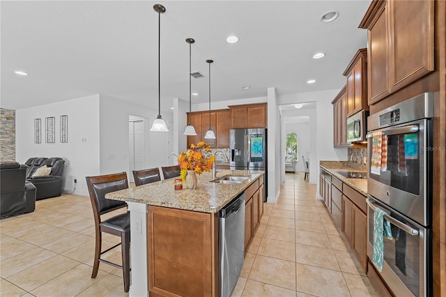 kitchen featuring stainless steel appliances, a center island with sink, sink, a breakfast bar, and pendant lighting