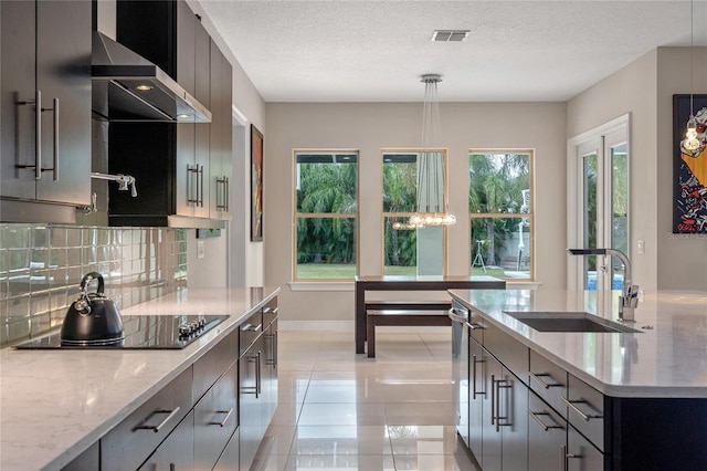 kitchen with tasteful backsplash, wall chimney exhaust hood, black electric cooktop, sink, and decorative light fixtures