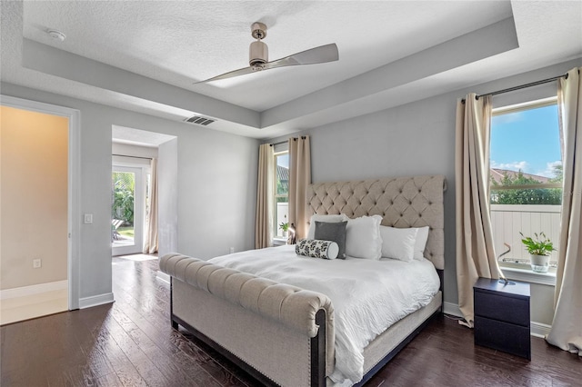 bedroom with dark wood-type flooring, ceiling fan, access to exterior, a textured ceiling, and a tray ceiling