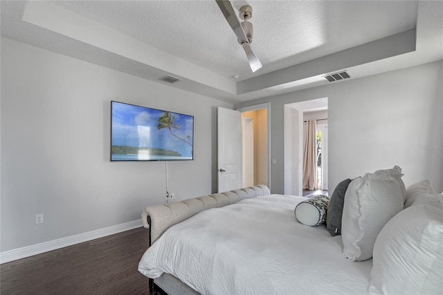 bedroom featuring a raised ceiling, ceiling fan, dark wood-type flooring, and a textured ceiling