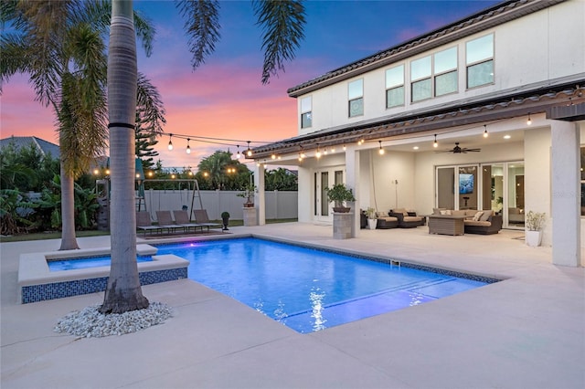 pool at dusk featuring ceiling fan, a patio area, an outdoor hangout area, and an in ground hot tub