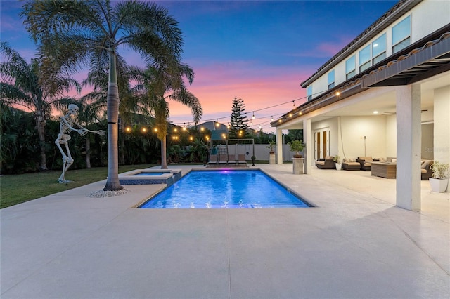 pool at dusk with a patio area, an outdoor hangout area, and an in ground hot tub