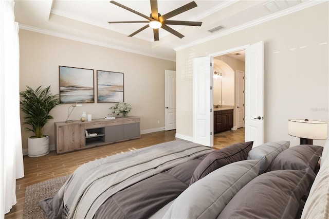 bedroom with a raised ceiling, ensuite bath, ceiling fan, and crown molding