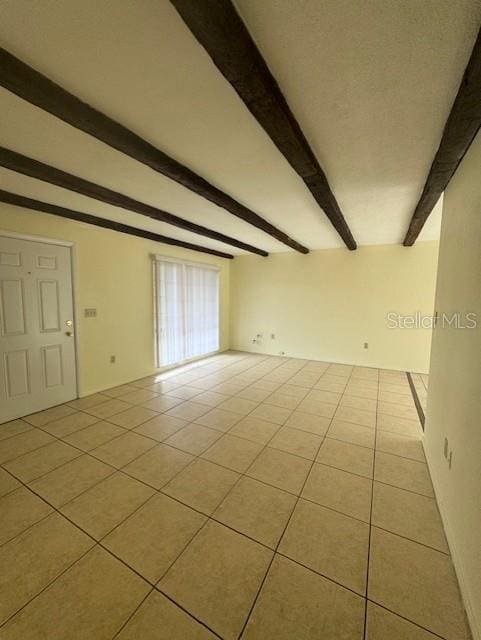 tiled empty room featuring beamed ceiling