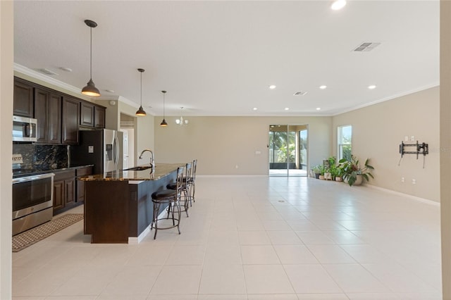 kitchen with dark brown cabinetry, stainless steel appliances, a center island with sink, and dark stone countertops