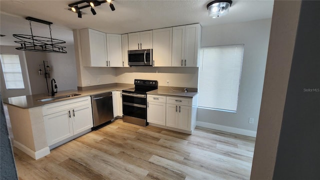 kitchen with white cabinets, light wood-style flooring, appliances with stainless steel finishes, hanging light fixtures, and a sink