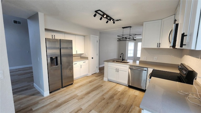 kitchen with white cabinets, hanging light fixtures, sink, light wood-type flooring, and appliances with stainless steel finishes