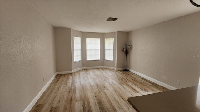 unfurnished room with a textured wall, light wood finished floors, and baseboards