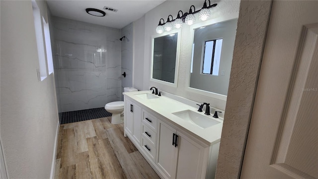 bathroom with double vanity, wood finished floors, a sink, and a marble finish shower